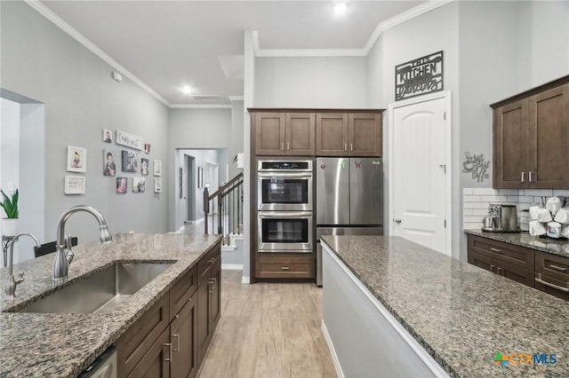 kitchen featuring sink, appliances with stainless steel finishes, dark stone countertops, dark brown cabinets, and light wood-type flooring