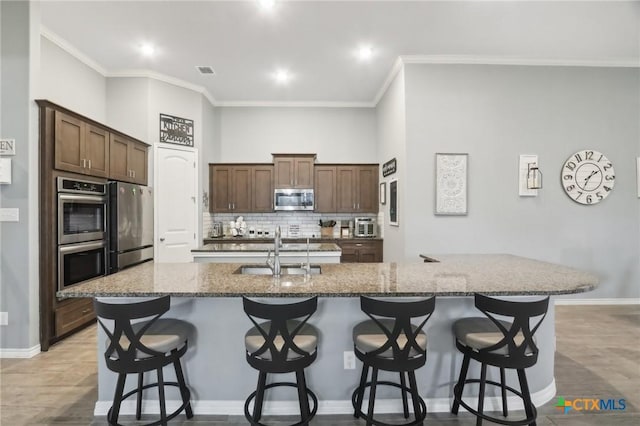 kitchen with appliances with stainless steel finishes, a kitchen breakfast bar, sink, and a center island with sink