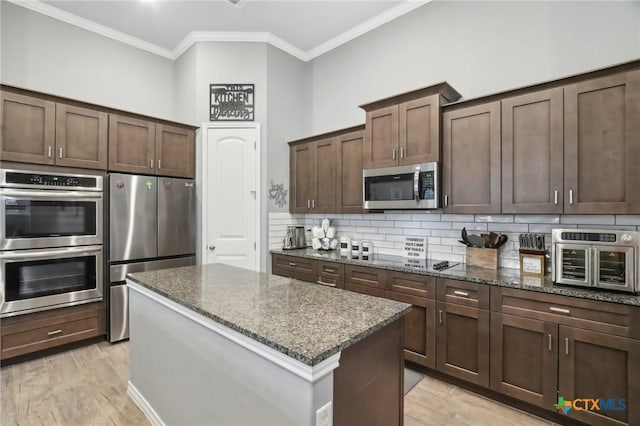 kitchen with dark stone countertops, stainless steel appliances, ornamental molding, a kitchen island, and decorative backsplash