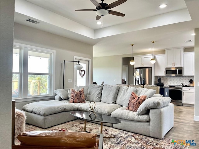 living room featuring light hardwood / wood-style flooring, ceiling fan, and a tray ceiling