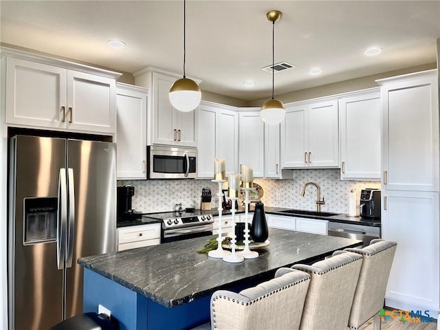 kitchen featuring a kitchen bar, sink, decorative light fixtures, stainless steel appliances, and white cabinets