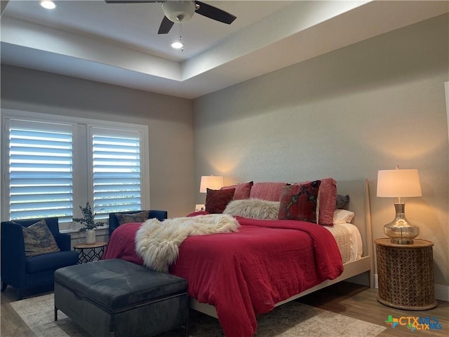 bedroom featuring a raised ceiling, ceiling fan, and light wood-type flooring