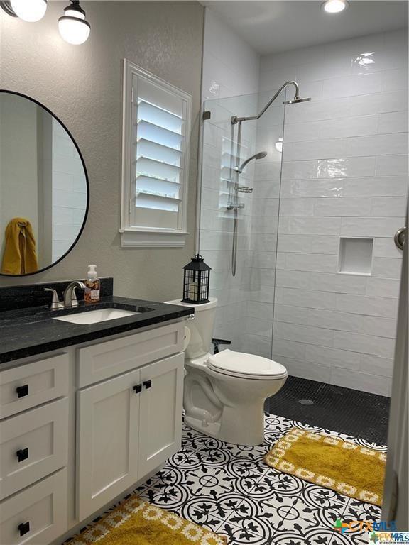 bathroom with tile patterned flooring, vanity, tiled shower, and toilet