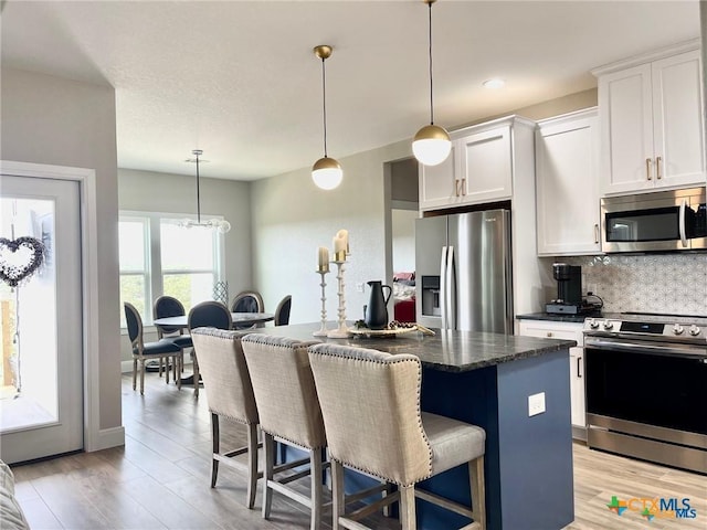 kitchen with pendant lighting, a breakfast bar, stainless steel appliances, white cabinets, and a kitchen island