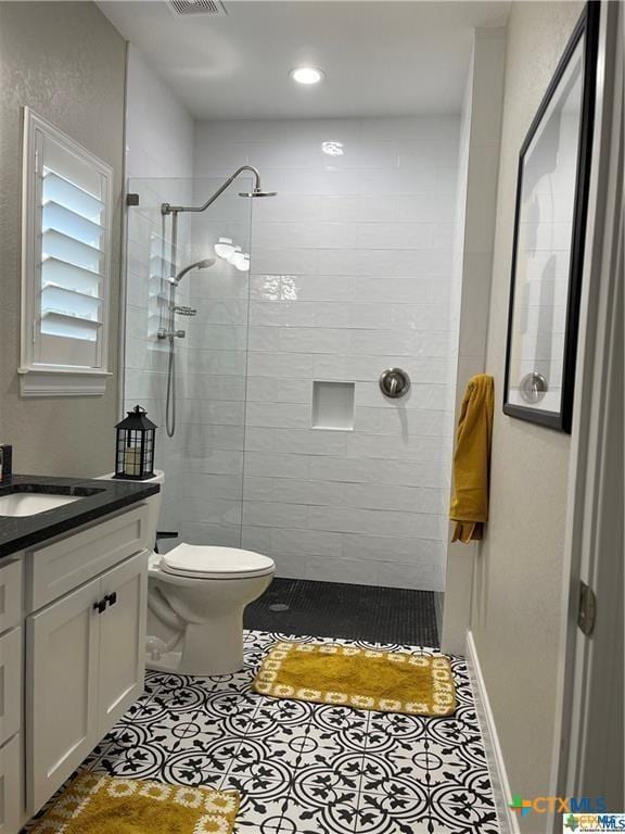 bathroom featuring tile patterned flooring, vanity, tiled shower, and toilet