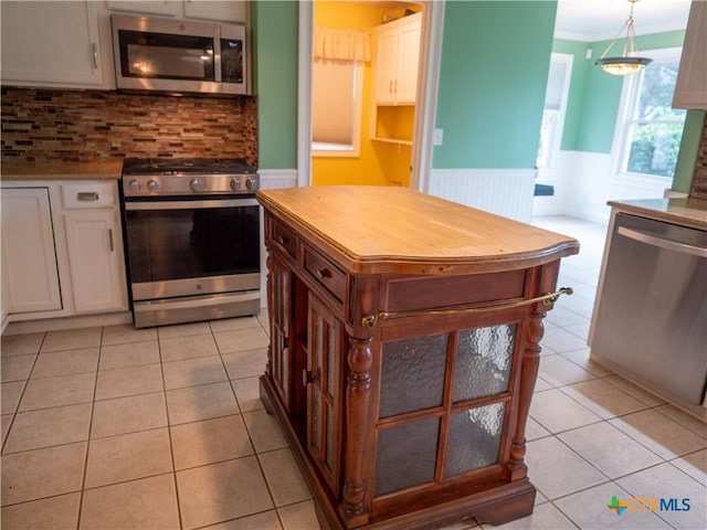 kitchen featuring backsplash, wainscoting, light tile patterned floors, stainless steel appliances, and white cabinetry