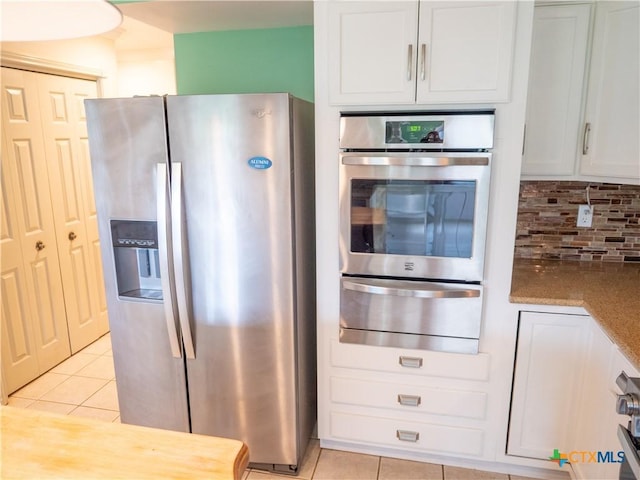 kitchen with a warming drawer, light tile patterned floors, white cabinets, appliances with stainless steel finishes, and backsplash