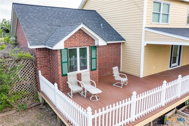 rear view of house with roof with shingles, a wooden deck, and brick siding