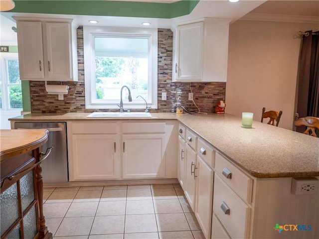kitchen with a peninsula, dishwasher, white cabinets, a sink, and backsplash