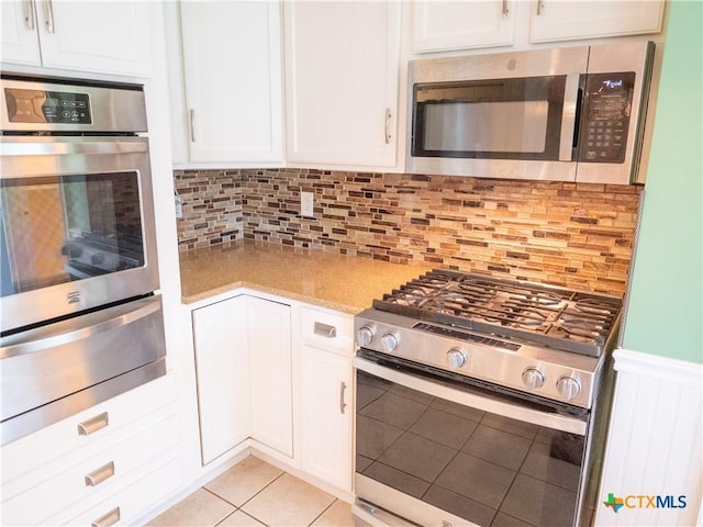 kitchen featuring tasteful backsplash, white cabinets, a warming drawer, stainless steel appliances, and light tile patterned flooring