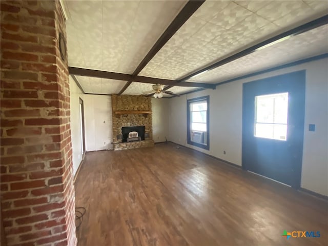 unfurnished living room featuring beamed ceiling, ceiling fan, wood finished floors, a stone fireplace, and coffered ceiling