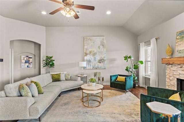 living room with vaulted ceiling, a stone fireplace, wood-type flooring, and ceiling fan