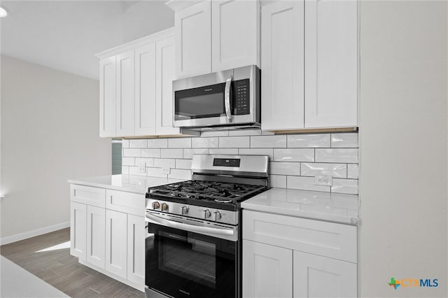 kitchen featuring backsplash, white cabinetry, wood-type flooring, and appliances with stainless steel finishes