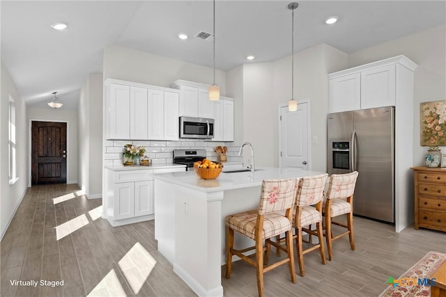 kitchen with appliances with stainless steel finishes, an island with sink, white cabinetry, sink, and hanging light fixtures