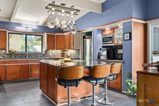 kitchen with stainless steel appliances, a kitchen island, backsplash, a kitchen bar, and sink