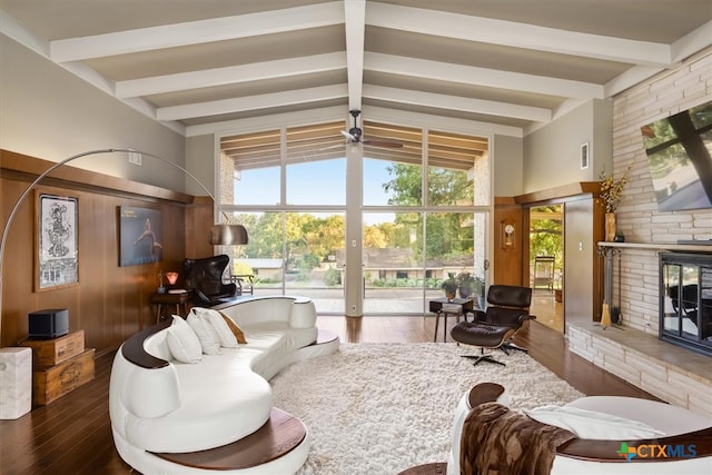 living room featuring ceiling fan, hardwood / wood-style flooring, a stone fireplace, and vaulted ceiling with beams