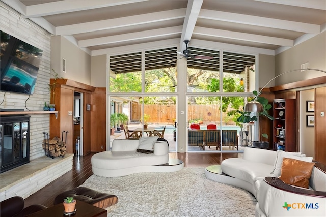 living room featuring a stone fireplace, lofted ceiling with beams, a wealth of natural light, and dark wood-type flooring