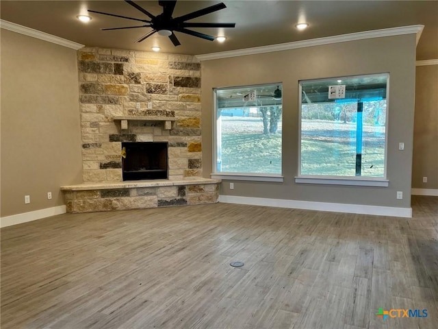 unfurnished living room with a wealth of natural light, a stone fireplace, ceiling fan, and crown molding