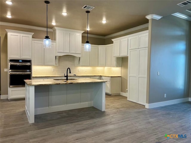 kitchen featuring light stone countertops, sink, decorative light fixtures, a center island with sink, and white cabinetry