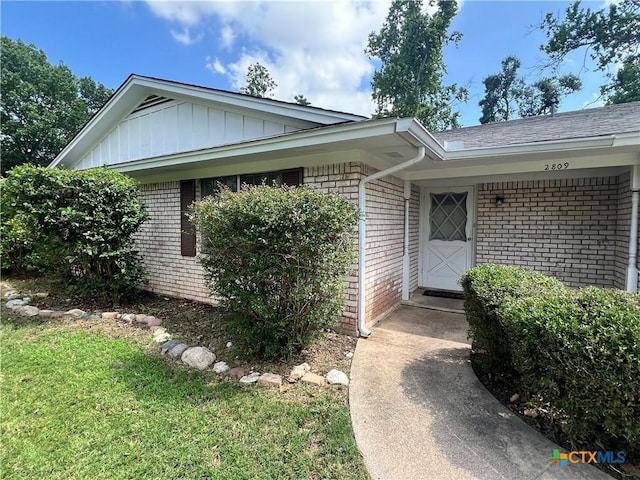 2809 Forest Trl, Temple, TX 76502 - view of exterior entry featuring brick siding, board and batten siding, roof with shingles, and a yard