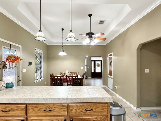 kitchen with light tile patterned flooring, ceiling fan, crown molding, and a tray ceiling