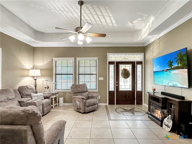 tiled living room featuring ornamental molding, a tray ceiling, and ceiling fan