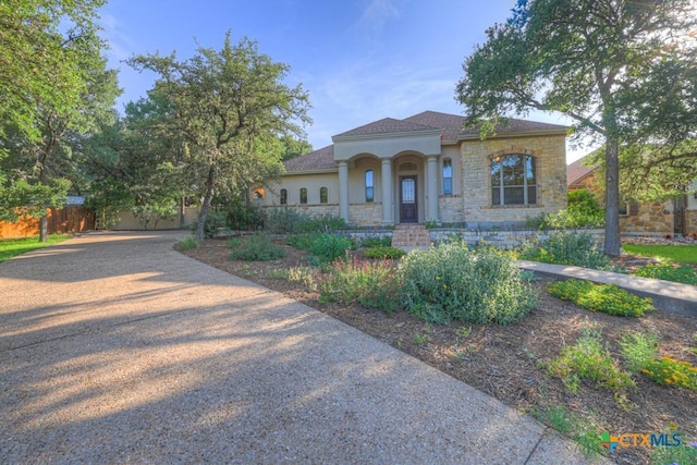 mediterranean / spanish-style home with stucco siding, fence, driveway, and stone siding