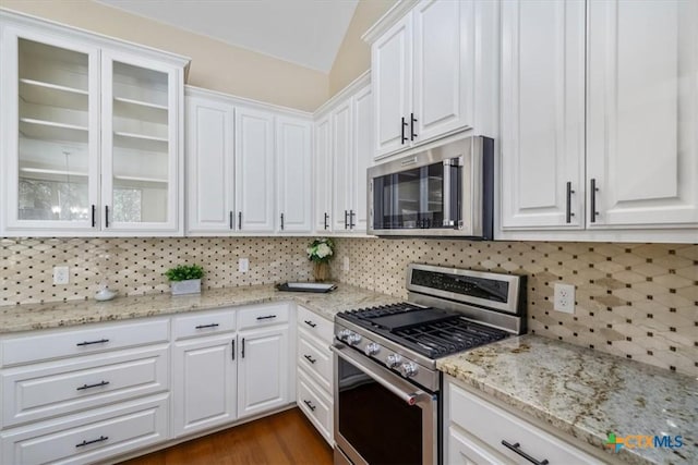 4012 Turning Leaf Dr, Nolanville, TX 76559 - kitchen featuring stainless steel appliances, white cabinets, decorative backsplash, glass insert cabinets, and vaulted ceiling