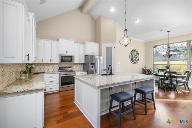 kitchen featuring sink, hanging light fixtures, stainless steel appliances, white cabinets, and an island with sink