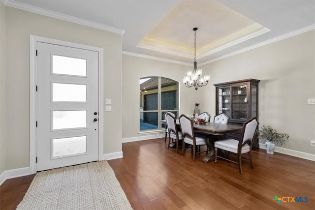 dining space with a tray ceiling, ornamental molding, dark wood-type flooring, and a chandelier