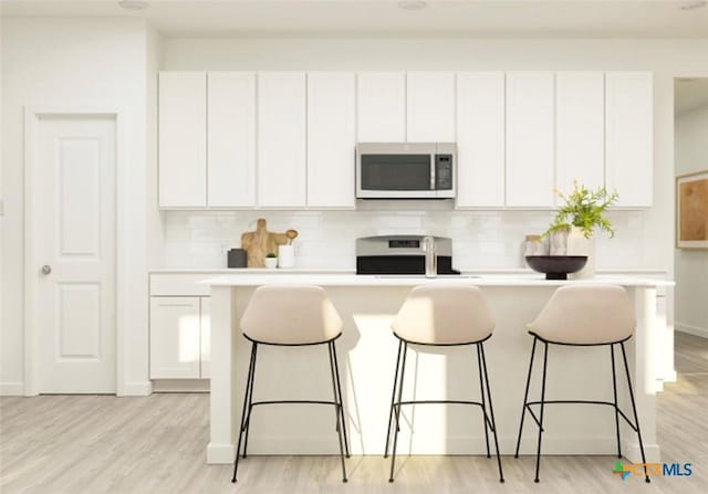 kitchen featuring an island with sink, stove, white cabinets, and light wood-type flooring