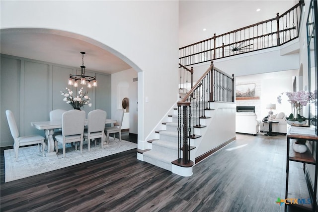 interior space with an inviting chandelier, a high ceiling, arched walkways, and wood finished floors