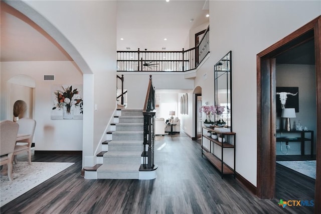 foyer entrance with arched walkways, a high ceiling, wood finished floors, visible vents, and baseboards