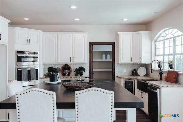 kitchen with double oven, dishwashing machine, a kitchen island, a sink, and white cabinetry