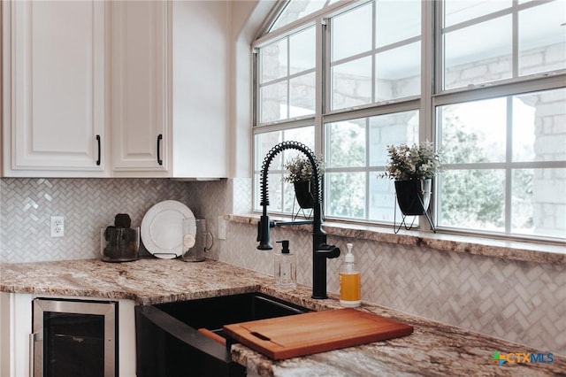 kitchen with tasteful backsplash, wine cooler, white cabinets, and light stone countertops