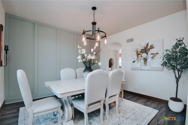 dining area featuring arched walkways, dark wood-type flooring, visible vents, baseboards, and an inviting chandelier