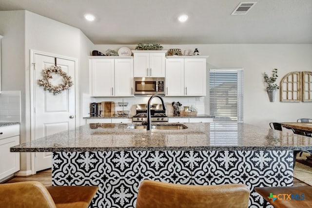 31696 Bard Ln, Bulverde, TX 78163 - kitchen featuring stainless steel microwave, a sink, a center island with sink, white cabinets, and dark stone counters