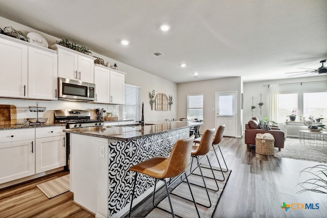 31696 Bard Ln, Bulverde, TX 78163 - kitchen with stainless steel appliances, a breakfast bar area, light wood-type flooring, dark stone counters, and recessed lighting
