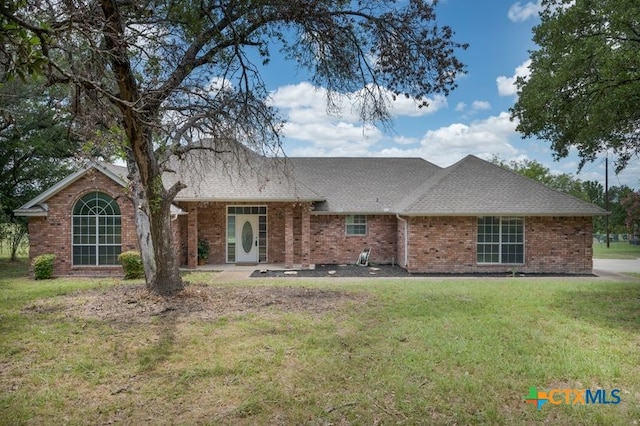 single story home with a shingled roof, a front yard, and brick siding