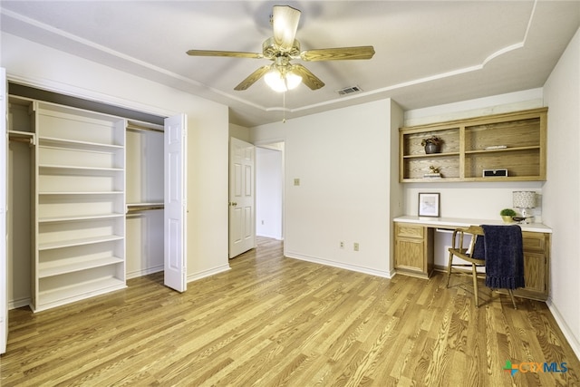 office space with visible vents, baseboards, built in desk, ceiling fan, and light wood-style flooring