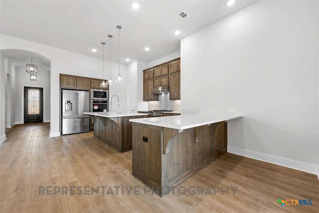kitchen with appliances with stainless steel finishes, a breakfast bar area, light countertops, baseboards, and light wood-type flooring