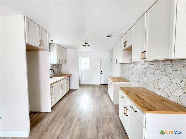 kitchen with visible vents, wooden counters, tasteful backsplash, a sink, and light wood-type flooring