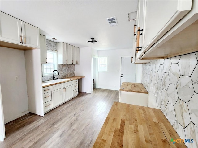 kitchen with butcher block countertops, a sink, tasteful backsplash, and visible vents