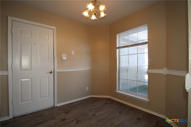 spare room featuring plenty of natural light, dark hardwood / wood-style floors, and an inviting chandelier