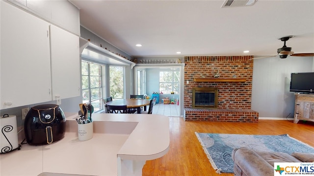 living room featuring light wood-type flooring, a brick fireplace, and ceiling fan