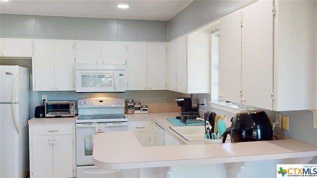 kitchen featuring white cabinetry, sink, a kitchen breakfast bar, kitchen peninsula, and white appliances