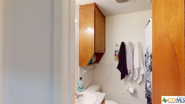 bathroom with vanity, toilet, and tile walls