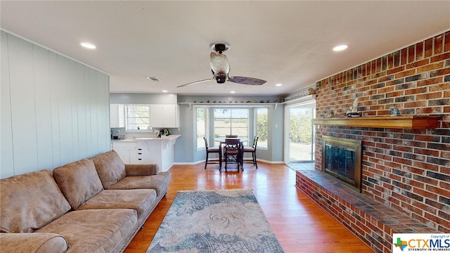 living room featuring ceiling fan, light hardwood / wood-style floors, and a brick fireplace