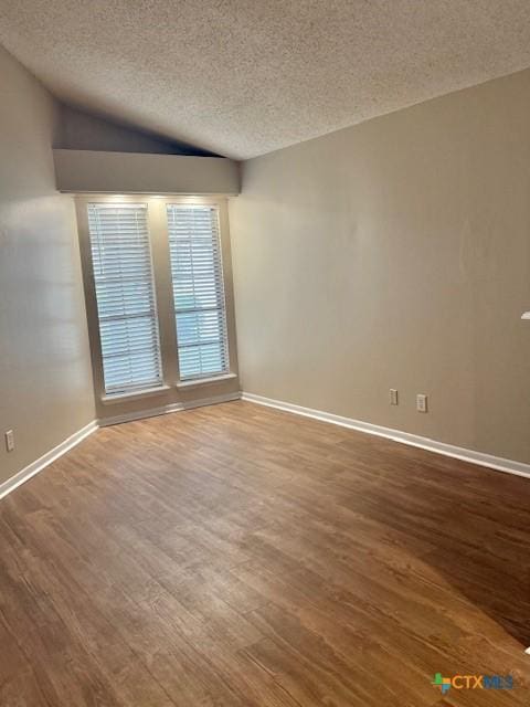 empty room with a textured ceiling, baseboards, vaulted ceiling, and wood finished floors