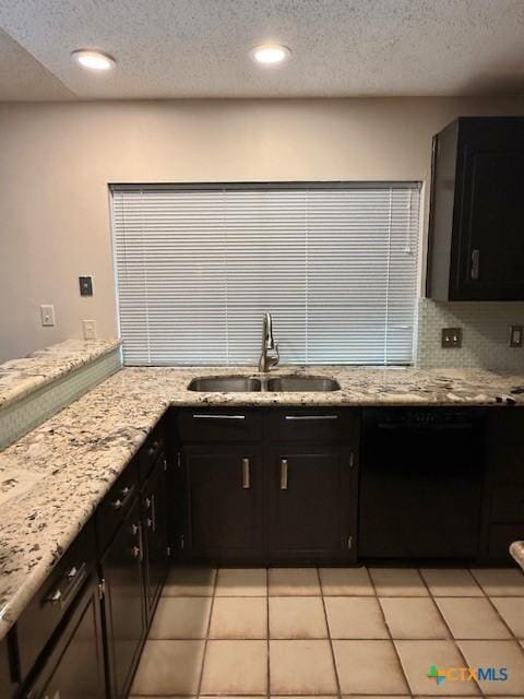 kitchen featuring tasteful backsplash, dark cabinetry, a sink, and light stone counters